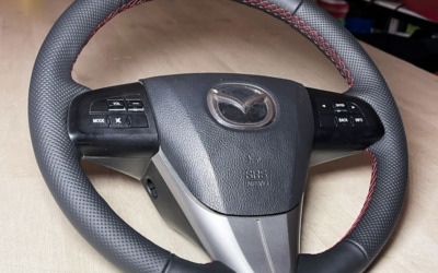 Перетянули руль Mazda 3 в натуральную кожу со вставками из псевдоперфорации, украсили красной сочной строчкой.